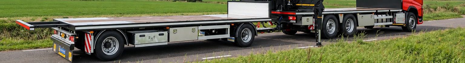Vrachtwagen met laadkraan en een lege oplegger op een dijkweg tussen de weilanden